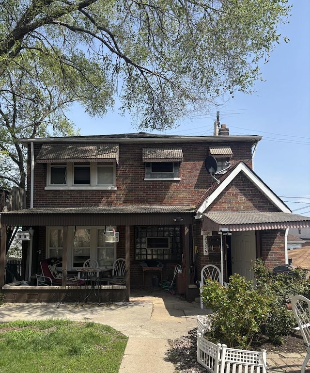 back of house featuring brick siding, covered porch, and a chimney