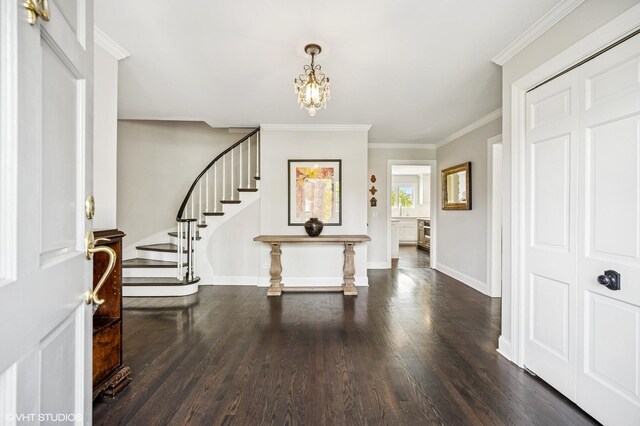 foyer with wood finished floors, a notable chandelier, stairway, baseboards, and ornamental molding