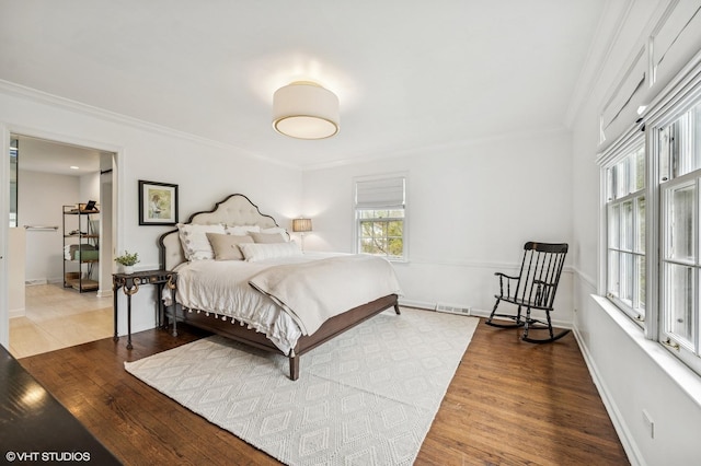 bedroom featuring baseboards, ornamental molding, visible vents, and wood finished floors