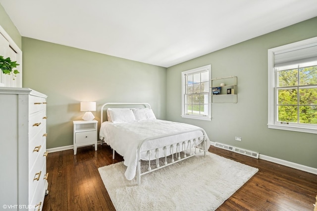 bedroom featuring baseboards, multiple windows, visible vents, and wood finished floors