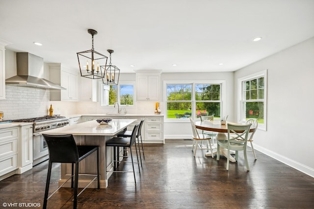 kitchen featuring tasteful backsplash, wall chimney exhaust hood, high end stove, light countertops, and baseboards