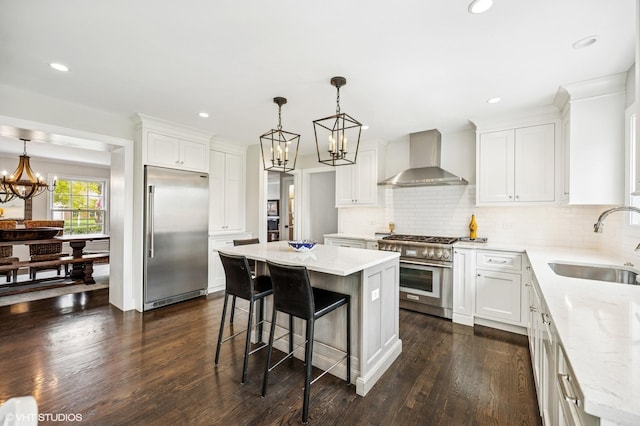 kitchen with a notable chandelier, a sink, white cabinetry, high end appliances, and wall chimney exhaust hood