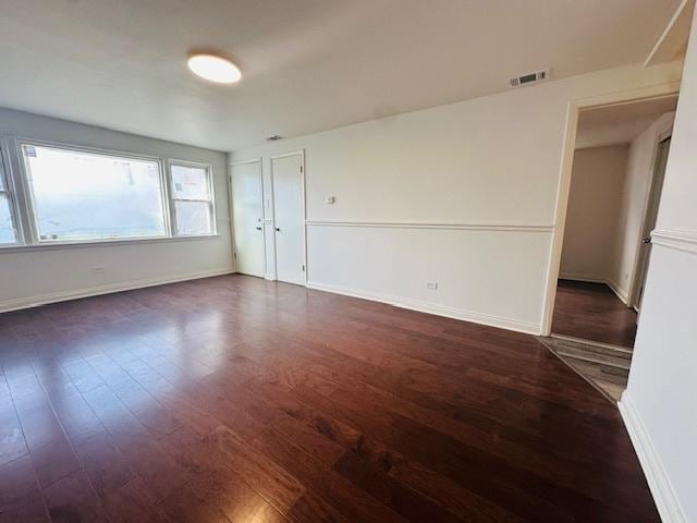 unfurnished room with dark wood-style flooring, baseboards, and visible vents