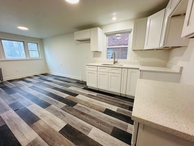kitchen with white cabinets, light stone counters, a sink, baseboards, and wood finished floors