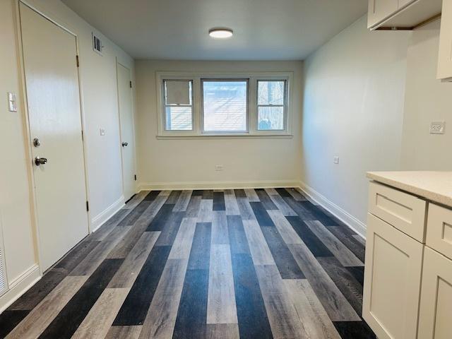 unfurnished dining area with visible vents, baseboards, and dark wood-style floors