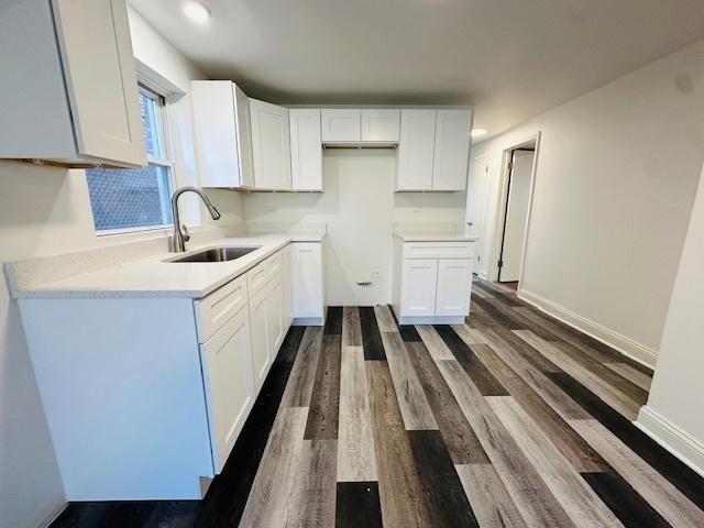 kitchen featuring white cabinets, a sink, light countertops, dark wood finished floors, and baseboards