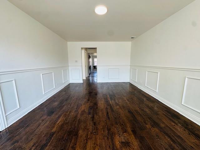 spare room featuring a decorative wall, dark wood-style floors, and a wainscoted wall