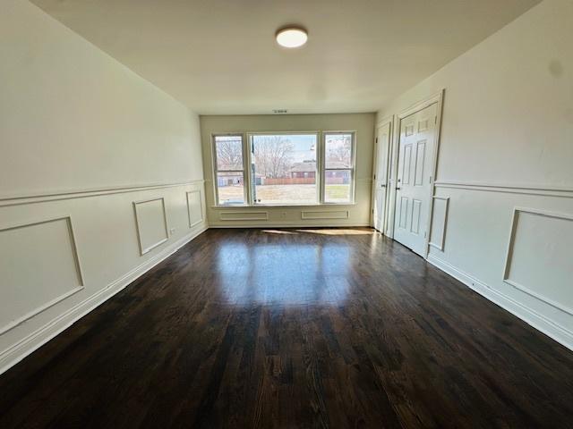 empty room featuring dark wood-style flooring, a decorative wall, and wainscoting