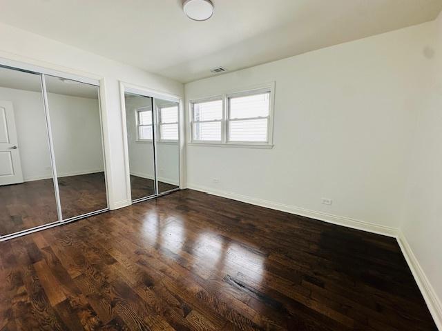 unfurnished bedroom featuring multiple closets, baseboards, wood finished floors, and visible vents