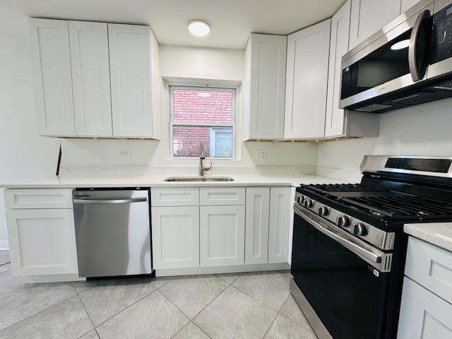 kitchen with appliances with stainless steel finishes, a sink, light tile patterned floors, white cabinets, and light countertops
