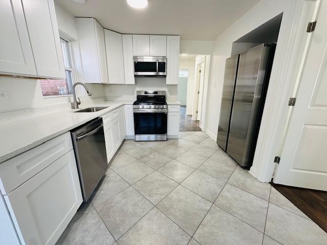 kitchen with white cabinets, light tile patterned flooring, a sink, light countertops, and stainless steel appliances