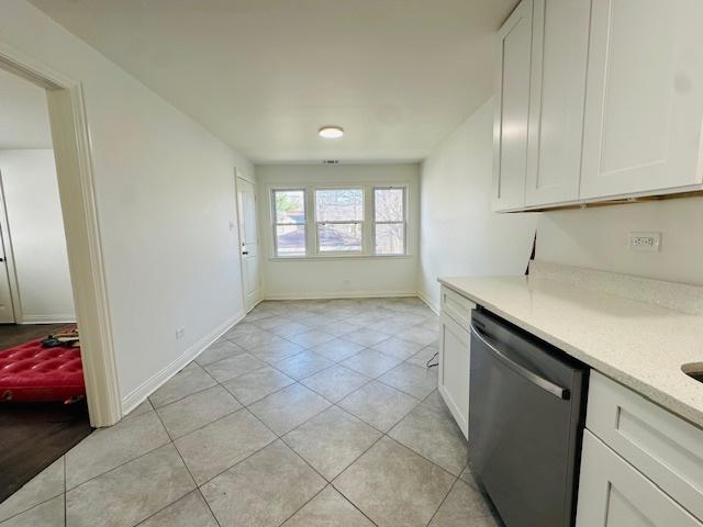 kitchen with stainless steel dishwasher, light countertops, light tile patterned floors, baseboards, and white cabinetry