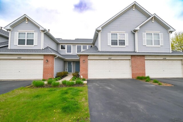 view of property featuring brick siding, aphalt driveway, an attached garage, and a front yard
