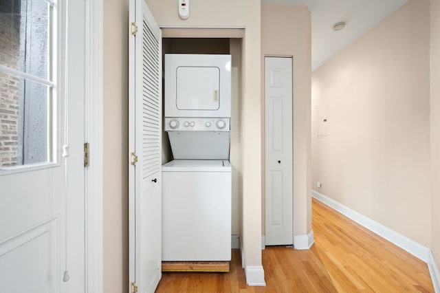 laundry area featuring baseboards, laundry area, light wood finished floors, and stacked washer and clothes dryer