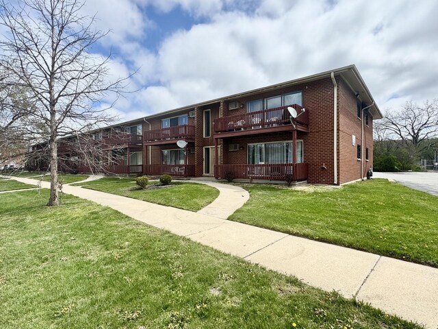 view of front facade featuring a balcony, a front lawn, and brick siding