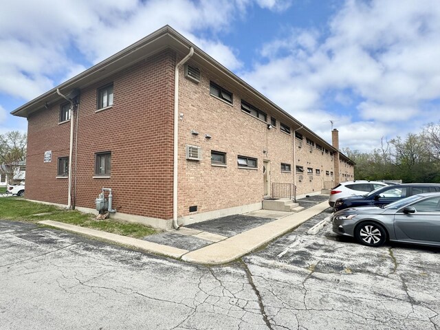 view of home's exterior with brick siding, uncovered parking, and a wall mounted air conditioner