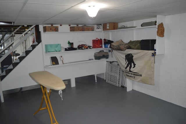 finished basement with concrete block wall, stairs, and a drop ceiling