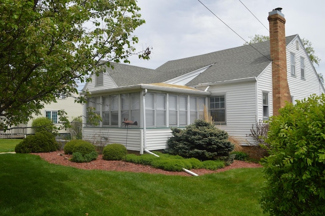 view of side of home with roof with shingles, a sunroom, a chimney, and a lawn