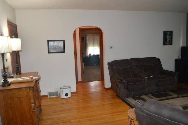 living area featuring arched walkways, light wood finished floors, and baseboards
