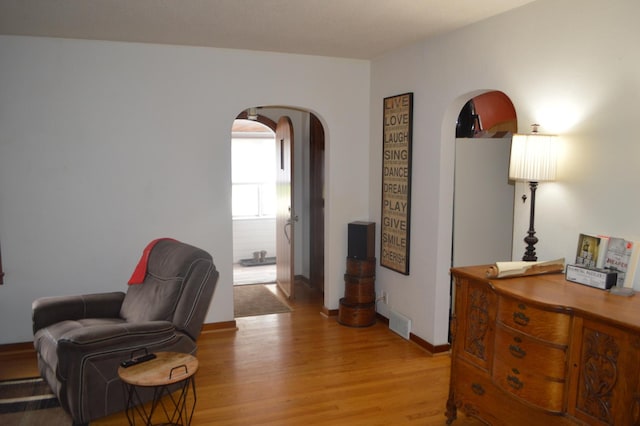 living area with arched walkways, light wood finished floors, and baseboards