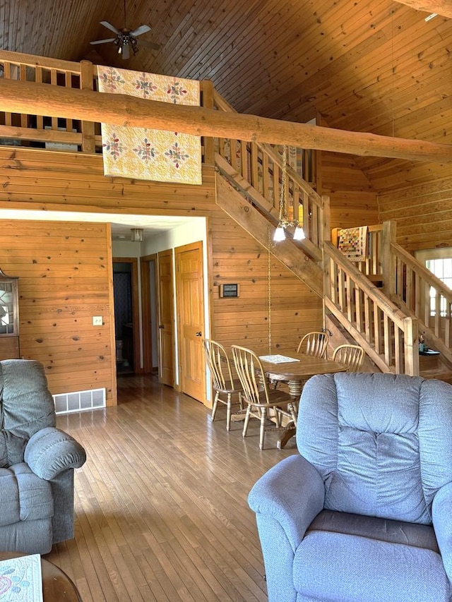 living area with high vaulted ceiling, wood walls, stairs, a ceiling fan, and visible vents