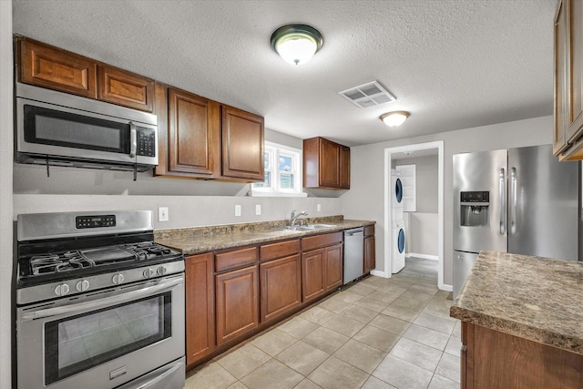 902 N Lincoln Ave, Urbana, IL 61801 - kitchen with stainless steel appliances, stacked washer / dryer, a sink, light tile patterned floors, and brown cabinets