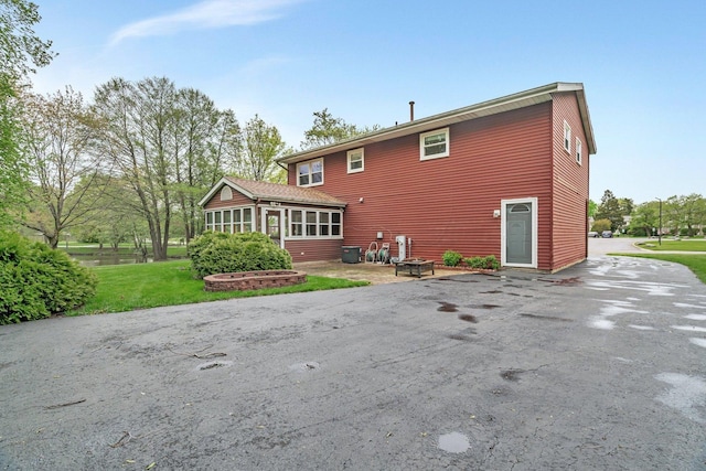 back of house featuring a lawn, central air condition unit, a sunroom, and driveway