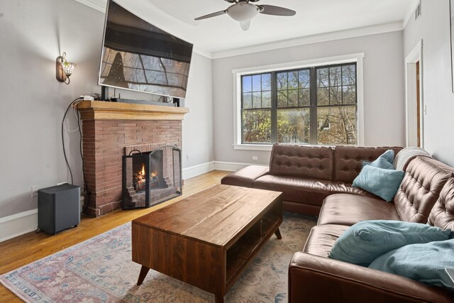 living room featuring a ceiling fan, a brick fireplace, wood finished floors, baseboards, and ornamental molding