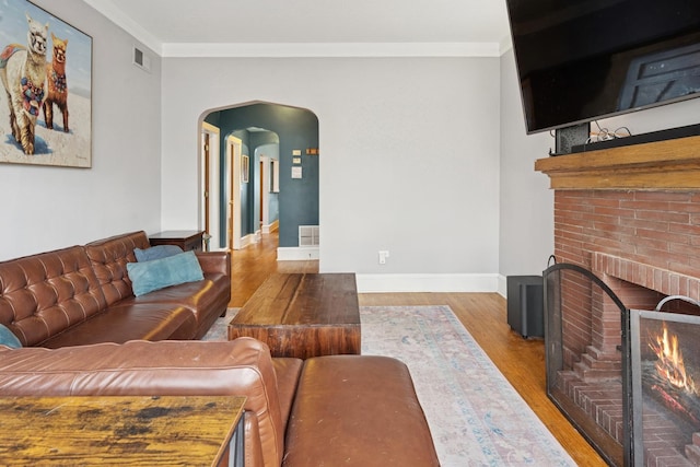 living area with crown molding, a brick fireplace, baseboards, wood finished floors, and visible vents