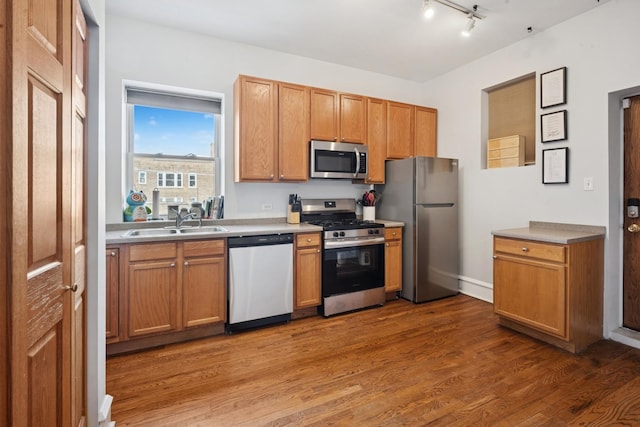 kitchen featuring appliances with stainless steel finishes, rail lighting, wood finished floors, a sink, and light countertops