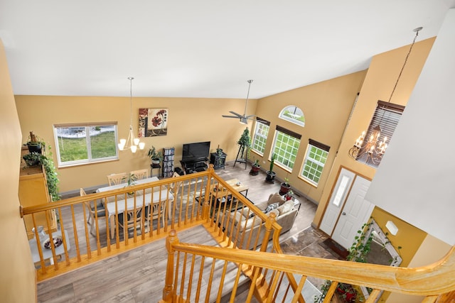 living room with high vaulted ceiling, plenty of natural light, wood finished floors, and ceiling fan with notable chandelier
