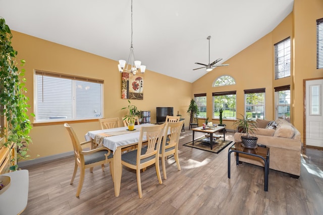 dining space featuring baseboards, ceiling fan with notable chandelier, wood finished floors, and high vaulted ceiling
