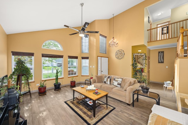 living room featuring baseboards, high vaulted ceiling, wood finished floors, and ceiling fan with notable chandelier