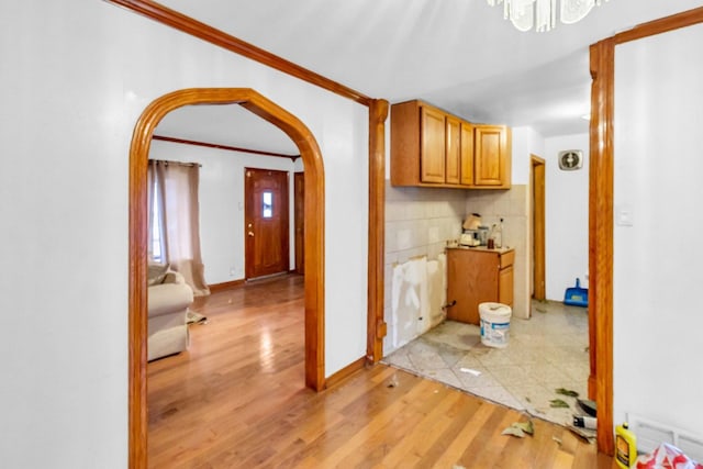 hall featuring light wood-style floors, arched walkways, a notable chandelier, and ornamental molding