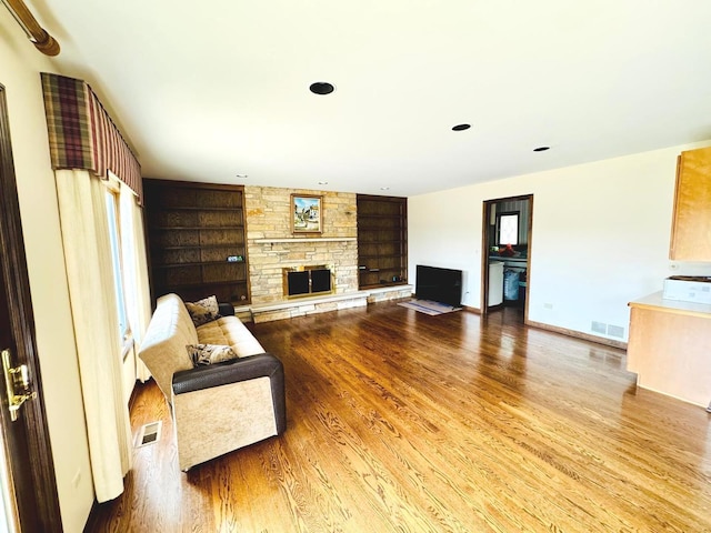 living area featuring visible vents, built in features, wood finished floors, and a fireplace