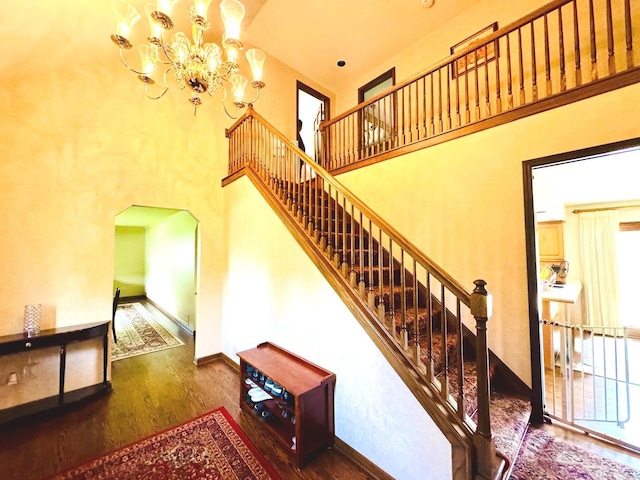 stairs featuring an inviting chandelier, arched walkways, a towering ceiling, and wood finished floors