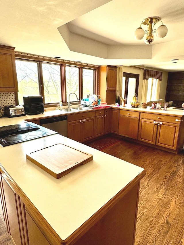 kitchen with stainless steel dishwasher, brown cabinets, dark wood finished floors, a sink, and a peninsula