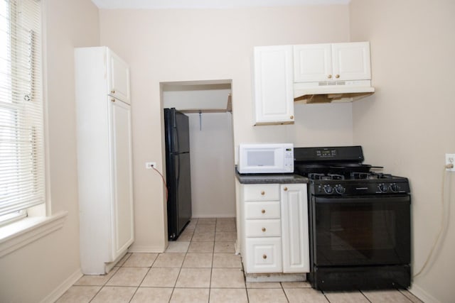 kitchen featuring dark countertops, white cabinetry, under cabinet range hood, light tile patterned floors, and black appliances