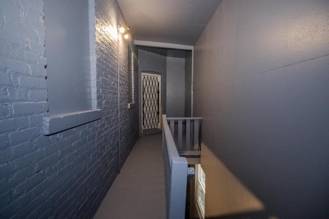hallway with brick wall, an upstairs landing, and concrete floors