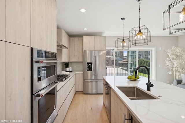 kitchen featuring light brown cabinets, light stone countertops, modern cabinets, a sink, and stainless steel appliances