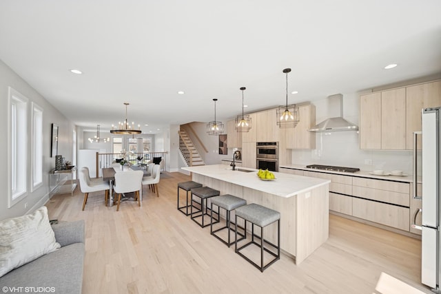 kitchen featuring wall chimney range hood, light brown cabinets, gas stovetop, a kitchen bar, and modern cabinets