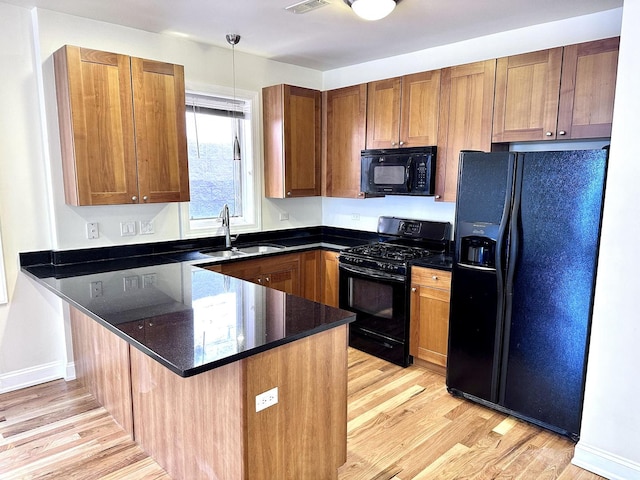 kitchen featuring brown cabinets, light wood-type flooring, a sink, black appliances, and a peninsula