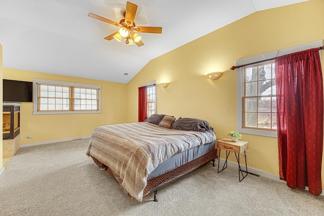 carpeted bedroom with baseboards, a glass covered fireplace, ceiling fan, and lofted ceiling