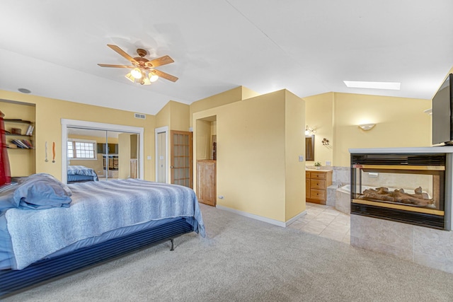 bedroom with light carpet, vaulted ceiling with skylight, ensuite bath, two closets, and visible vents