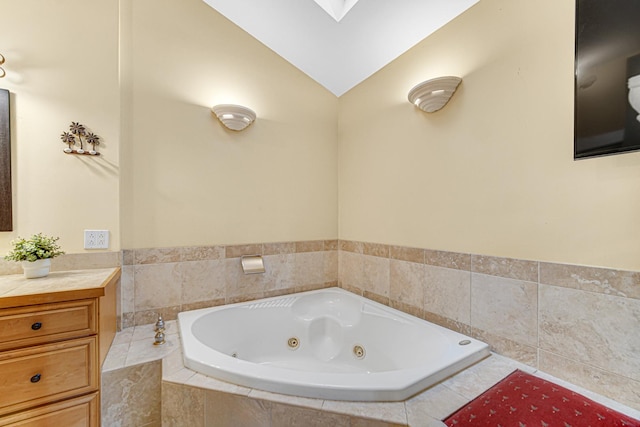 full bathroom with vanity, vaulted ceiling with skylight, and a jetted tub