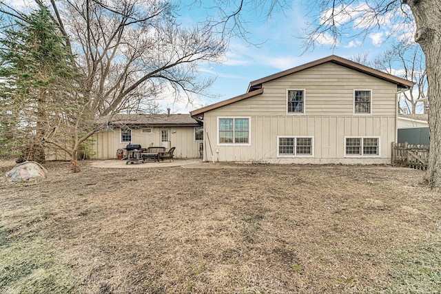 rear view of house with board and batten siding, a patio area, and fence