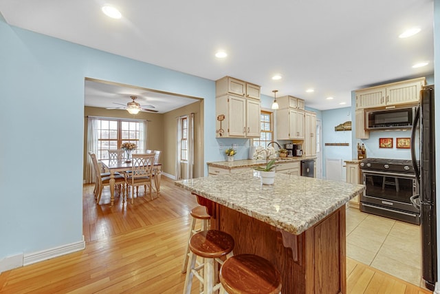 kitchen featuring ceiling fan, a breakfast bar, baseboards, light wood-type flooring, and black appliances