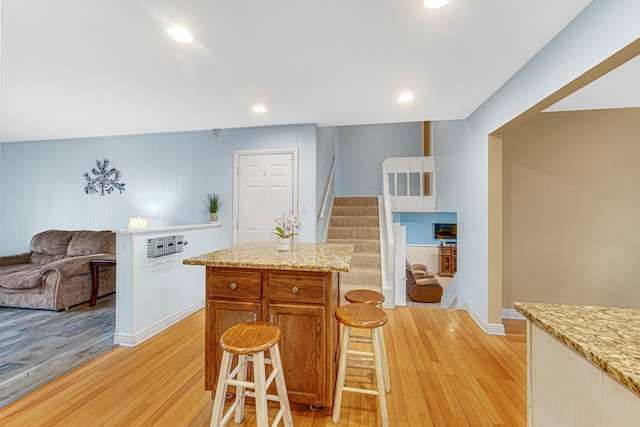 kitchen with a kitchen island, a breakfast bar, open floor plan, recessed lighting, and light wood finished floors
