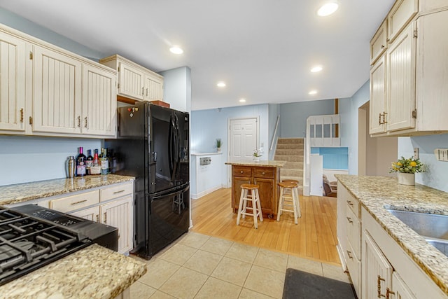 kitchen with recessed lighting, light stone counters, a sink, light tile patterned floors, and black fridge