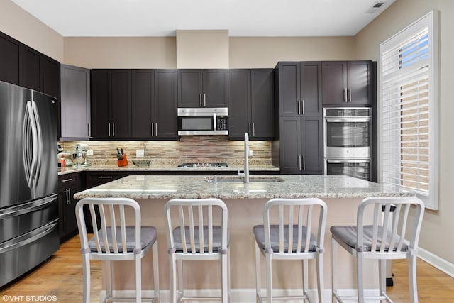 kitchen featuring a sink, appliances with stainless steel finishes, tasteful backsplash, and light wood finished floors